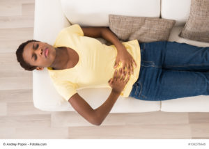 A woman laying on a couch with her stomach hurting.