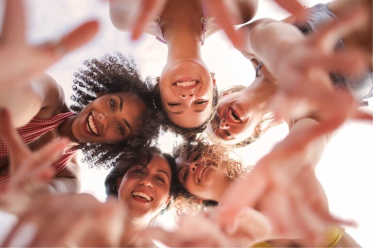 Looking up from the ground at a group of girls that are reaching down.