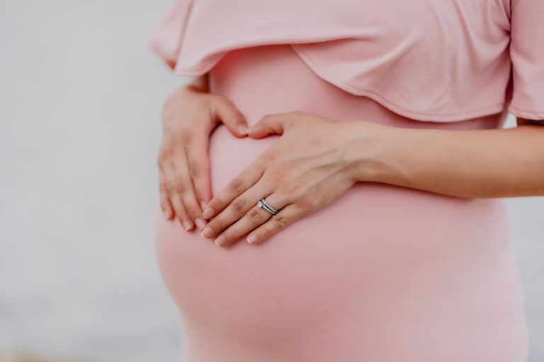 A pregnant woman with her hands on her belly in the shape of a heart.