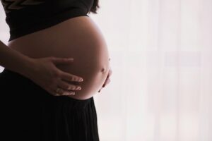 A pregnant woman is holding her belly in front of a window.